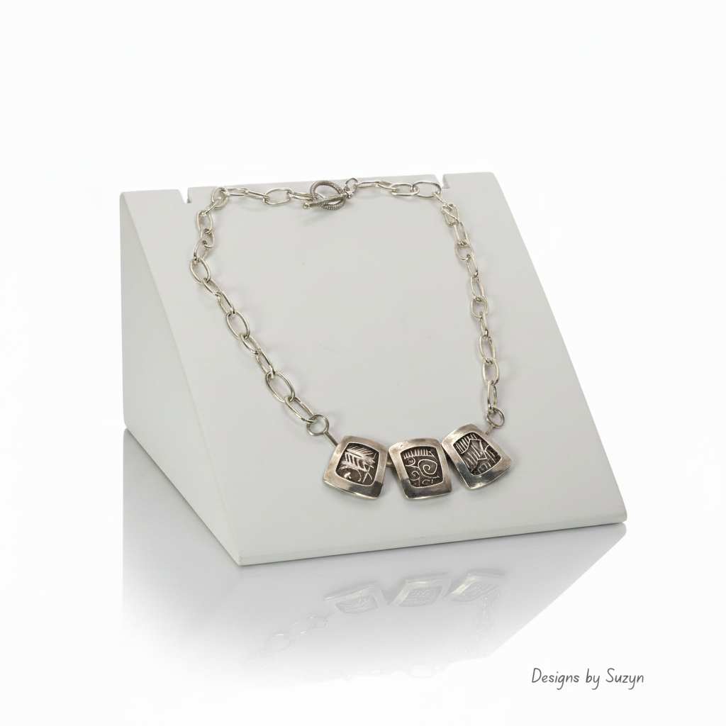Three-Panel Silver Necklace on Sloped Platform with Watermark